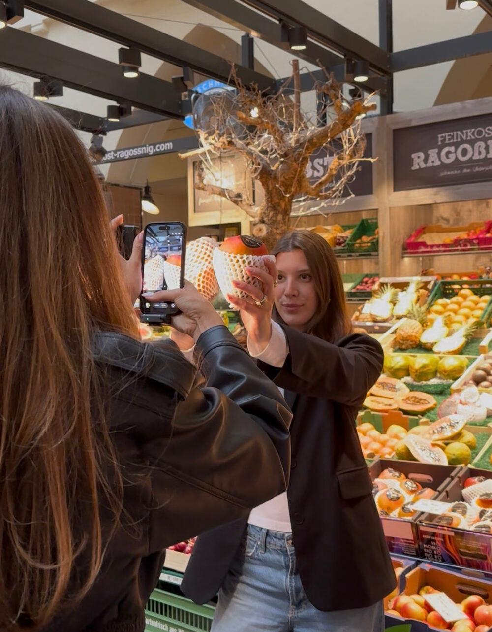 Eine Creatorin filmt eine andere mit dem Handy an einem Obststand